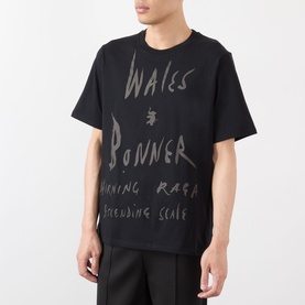 Model wearing Wales Bonner black cotton T-shirt with tonal handwritten-style graphic lettering print to front, styled with black trousers