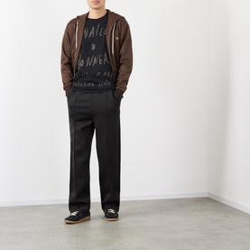 Model wearing Wales Bonner black graphic cotton T-shirt, styled with brown patterned zip hoodie, black wide-leg trousers and black shoes.