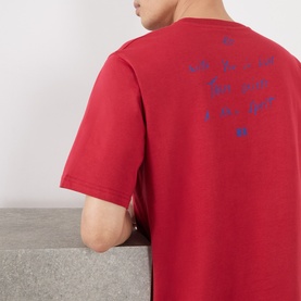 Model wearing Wales Bonner Raga Logo T-Shirt in Rooibois, showing blue logo lettering on back, crew neck, short sleeves