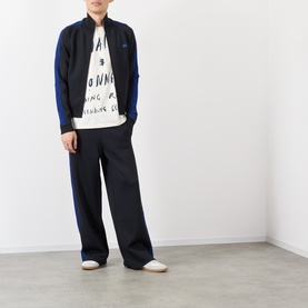 Model wearing Wales Bonner ivory cotton T-shirt with graphic print, styled with navy track jacket and wide-leg black trousers.