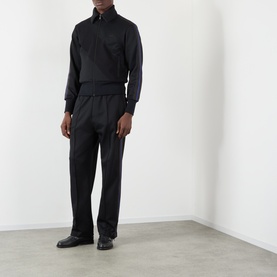 Model wearing Wales Bonner Form Logo Track Pants in black with contrast stripe detail, styled with matching black half-zip top and black leather