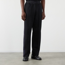 Model wearing Wales Bonner Form Logo Track Pants in black with contrast stripe detail along each leg, straight-leg fit, paired with black leather