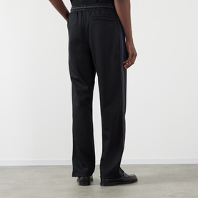 Model wearing Wales Bonner Form Logo Track Pants in black, showing rear view with contrast stripe detailing and straight-leg silhouette
