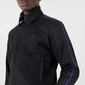 Model wearing Wales Bonner Form Logo Zip Track Sweatshirt in black with blue contrast arm stripe and gold logo embroidery at chest.