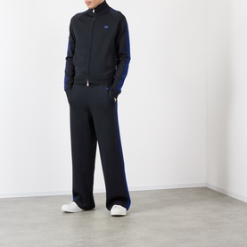 Model wearing black and navy zip-up track jacket with contrast side stripe, styled with matching wide-leg trousers and white trainers