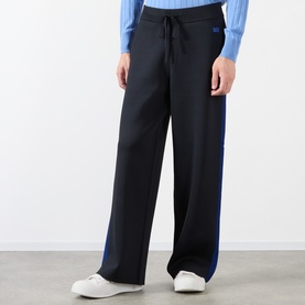 Model wearing black wide-leg trousers with blue side stripe and drawstring waist, styled with a light blue knit top and white trainers.