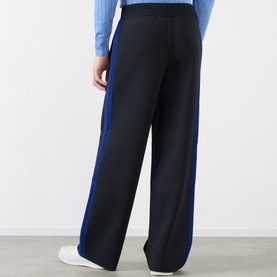 Model wearing black wide-leg trousers with blue side stripe detail, styled with a light blue top and white trainers.