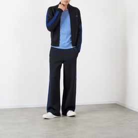 Model wearing navy and blue zip-up track jacket with wide-leg trousers and blue ribbed top, styled with white trainers