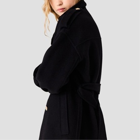 Model wearing Maje red wrap coat with wide lapels, self-tie belt, and gold-tone button detail, side view