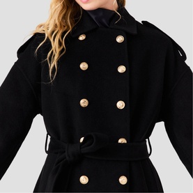Model wearing Maje red double-breasted coat with gold buttons, belted waist, and wide lapels