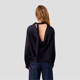Model wearing Maje top in navy with open cowl back detail and tie neck, styled with wide-leg dark denim jeans