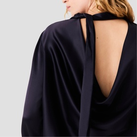 Model wearing Maje navy satin top with open cowl back, tie detail at neckline, and draped long sleeves