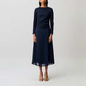 Model wearing Claude Pierlot blue long-sleeve top and matching navy pleated midi skirt, styled with gold strappy heeled sandals