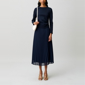 Model wearing Claude Pierlot blue long-sleeve top and matching pleated midi skirt, styled with gold heeled sandals and a white shoulder bag.