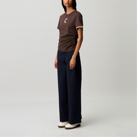 Model wearing Claude Pierlot brown fitted T-shirt with logo detail and white trim, styled with navy wide-leg trousers and white shoes.