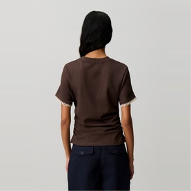 Model wearing Claude Pierlot brown short-sleeve top with contrast crochet trim cuffs, styled with navy trousers, seen from behind.