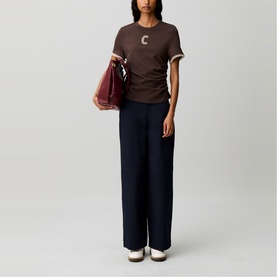 Model wearing Claude Pierlot brown graphic tee with white trim, styled with wide-leg navy trousers, carrying a burgundy bag