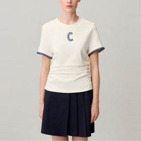 Model wearing Claude Pierlot cream short-sleeve top with navy embroidered moon motif and contrast stitched cuffs, styled with a navy mini skirt.