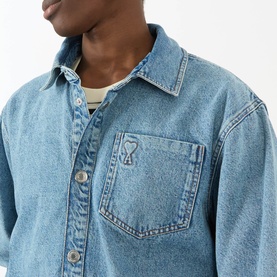 Model wearing AMI Casual Jacket in Bleu Used denim with chest pocket and embroidered Ami de Coeur logo, styled over cream top.