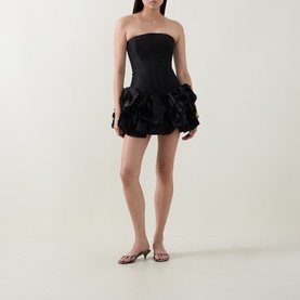 Model wearing Aje black strapless mini dress with voluminous floral ruffle skirt, styled with strappy kitten heel sandals