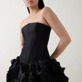 Model wearing Aje black strapless dress with structured corset bodice and voluminous ruffled organza skirt, styled with drop earrings.
