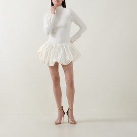 Model wearing Aje cream long-sleeve mini dress with fitted top and voluminous puffball skirt, styled with strappy heeled sandals