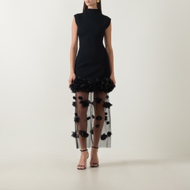 Model wearing Aje black sleeveless midi dress with high neck, structured bodice and sheer tulle skirt with 3D floral appliqu&eacute;s, styled with black