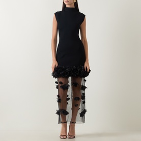 Model wearing Aje black midi dress with mock neck, cap sleeves and sheer floral 3D appliqu&eacute; hem detail, styled with strappy heels.
