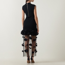 Model wearing Aje black dress, rear view, fitted bodice with sheer floral appliqu&eacute; skirt overlay and strappy heeled sandals.