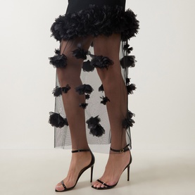 Model wearing Aje black sheer tulle dress with 3D floral appliqu&eacute;, styled with black strappy heeled sandals.