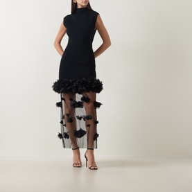 Model wearing Aje black sleeveless dress with ribbed bodice and sheer skirt with 3D floral appliqu&eacute; trim, styled with black strappy heels.