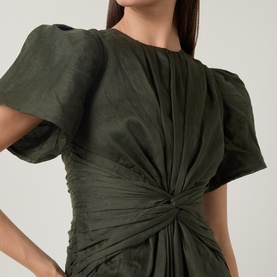 Model wearing Aje dark olive dress with puff sleeves, ruched twist-knot waist detail in lyocell-linen blend fabric