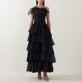 Model wearing Aje black tiered maxi dress with feather trim one-shoulder neckline and layered ruffled skirt, styled with strappy heels