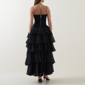 Model wearing Aje black tiered ruffle maxi dress with spaghetti straps, structured bodice, shown from behind with black heels.