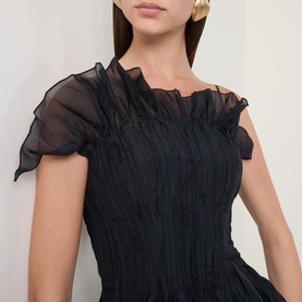 Model wearing Aje black dress with ruched bodice, sheer organza frill neckline and cap sleeves, paired with gold earrings