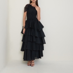 Model wearing Aje black tiered maxi dress with one-shoulder ruffle detail and layered skirt, styled with black strappy heels