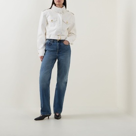 Model wearing Aje jeans in Stormy Wash, straight-leg denim, styled with a cream cropped jacket and black heeled mules.