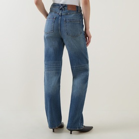 Model wearing Aje jeans in Stormy Wash, rear view showing relaxed straight-leg fit with faded denim detail, styled with black heeled mules