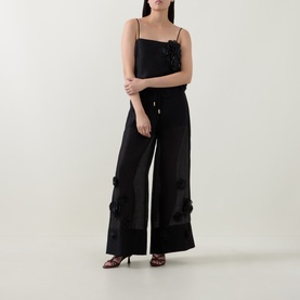 Model wearing Aje black cami top with floral appliqu&eacute; detail, styled with wide-leg black satin trousers and strappy heels.