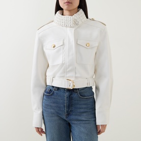 Model wearing Aje Mossan Utility Cropped Jacket in ivory with braided high neck, gold-toned hardware, patch pockets and removable belt, styled with