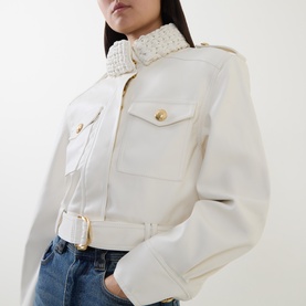 Model wearing Aje Mossan Utility Cropped Jacket in ivory with braided high neck, gold-toned hardware and patch pockets, styled with blue jeans