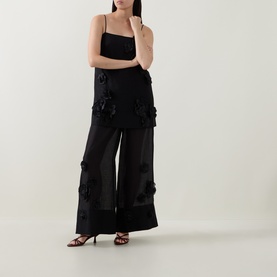 Model wearing Aje black cami top with 3D floral appliqu&eacute;, styled with matching wide-leg trousers and black heeled sandals.