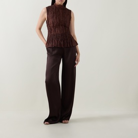 Model wearing Aje chocolate textured sleeveless peplum top with wide-leg dark trousers and open-toe heeled sandals.