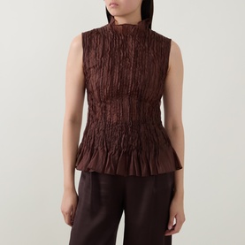 Model wearing Aje chocolate crinkle-textured sleeveless top with high neck and peplum hem, styled with dark brown wide-leg trousers