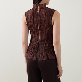 Model wearing Aje chocolate crinkle-textured sleeveless top, back view showing gold zip detail, styled with wide-leg trousers.