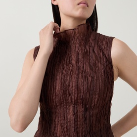 Model wearing Aje chocolate sleeveless crinkle-texture high-neck top, adjusting collar, cropped detail view.