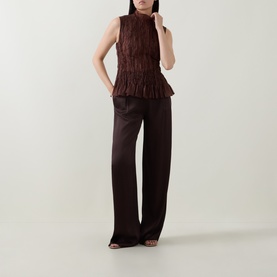 Model wearing Aje chocolate textured sleeveless top with ruffle hem, styled with wide-leg satin trousers in matching dark brown tone.