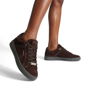 Model wearing Carvela brown suede lace-up trainers with gold branding detail and dark rubber sole