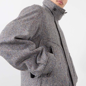 Model wearing Dries Van Noten black wool casual jacket with herringbone texture, high funnel neck and side pockets, close-up detail view.
