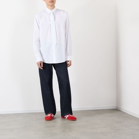 Model wearing Dries Van Noten white cotton casual shirt with dark navy jeans and red trainers.